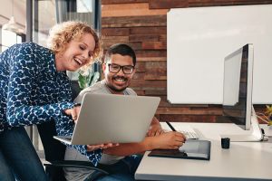 two colleagues look at laptop while smiling