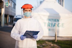 nurse in PPE with clipboard standing outside