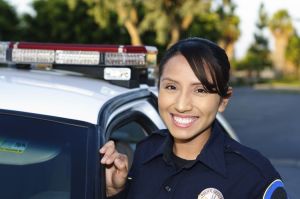 A smiling police officer stands beside her patrol car..
