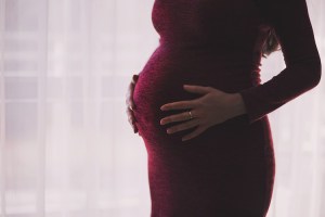 A pregnant mother in a maroon dress cradles her belly.