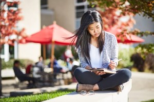 student sitting outdoors with tablet looking down
