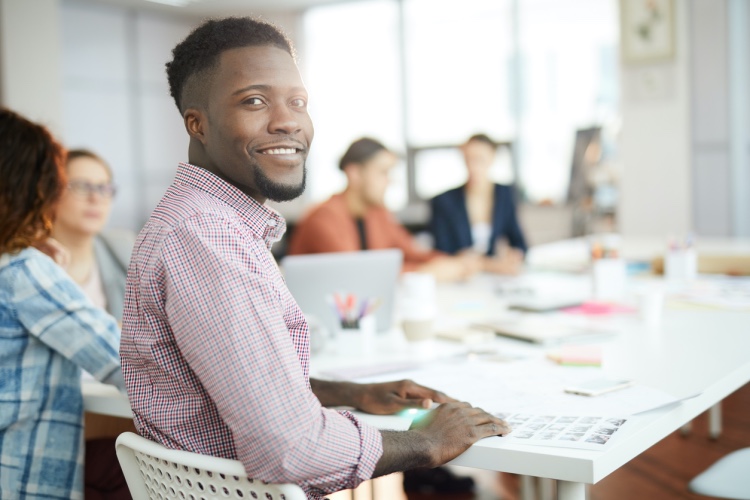 A young professional man sits at a conference table with his work colleagues