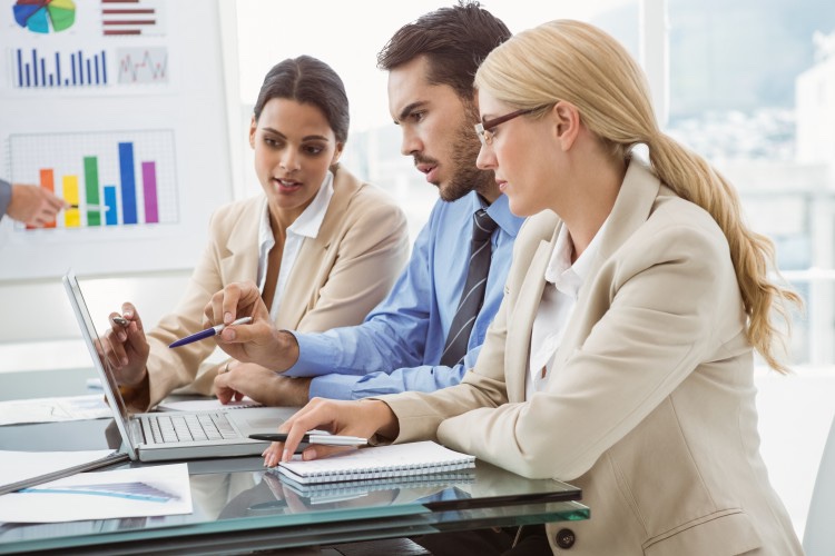 Coworkers discuss financial analytics while looking at a computer.