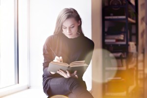 Woman reads a book and takes notes in a library.