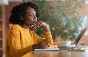 A woman in a yellow sweater sits at a table deep in thought.