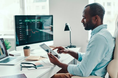 a man sitting in front of a computer looking at his tablet