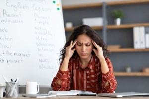 Teacher at a desk rubbing her temples and looking at a book.