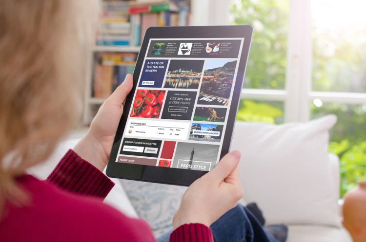 A person reading on a tablet sees article headlines and advertisements.