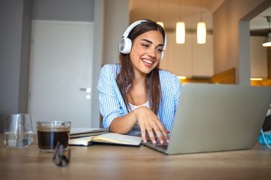 A student wearing headphones attends a virtual class meeting on a laptop.