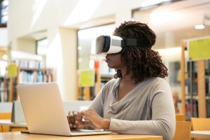 A student uses a VR headset and a laptop to attend online college.