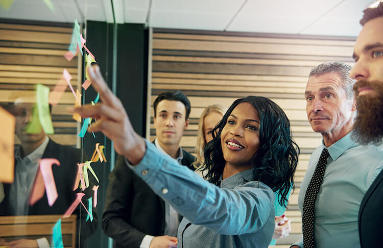 Organizational leader posting sticker on the board in front of her team. 