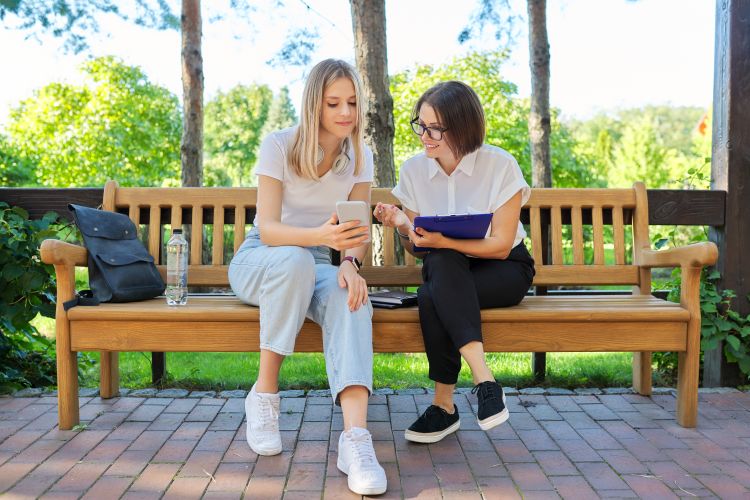 A university student and a career counselor are sitting on a bench discussing coursework and career plans.