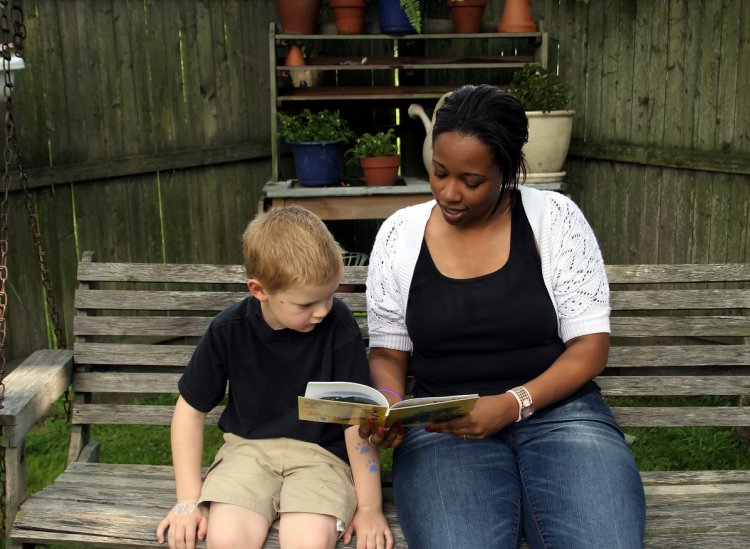 A child welfare social worker reads a book with a young child on a bench.
