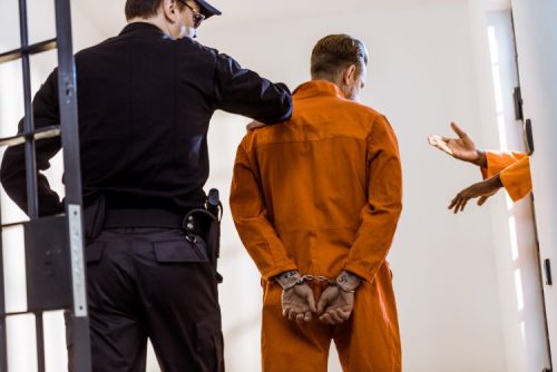 A corrections officer escorts an inmate through a prison hallway.