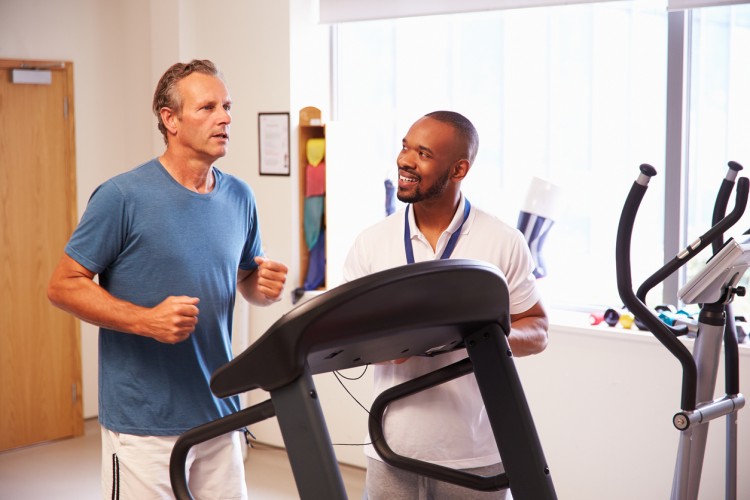 An exercise physiologist watches a man running on a treadmill in a hospital physical therapy department