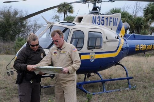 Two U.S. Fish & Wildlife Service officers look at a map in front of a helicopter.