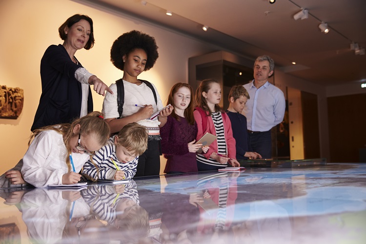 A historian shows a group of children a display during a tour of a museum.