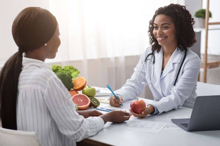 A nutritionist in a white coat holds an apple during a consultation with a client