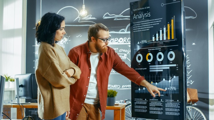 Two statisticians analyze financial data on a display.