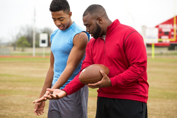 An athletic development specialist shows a young athlete how to carry a football.