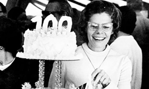 Centennial Timeline - Woman enjoying birthday cake with 100 candle