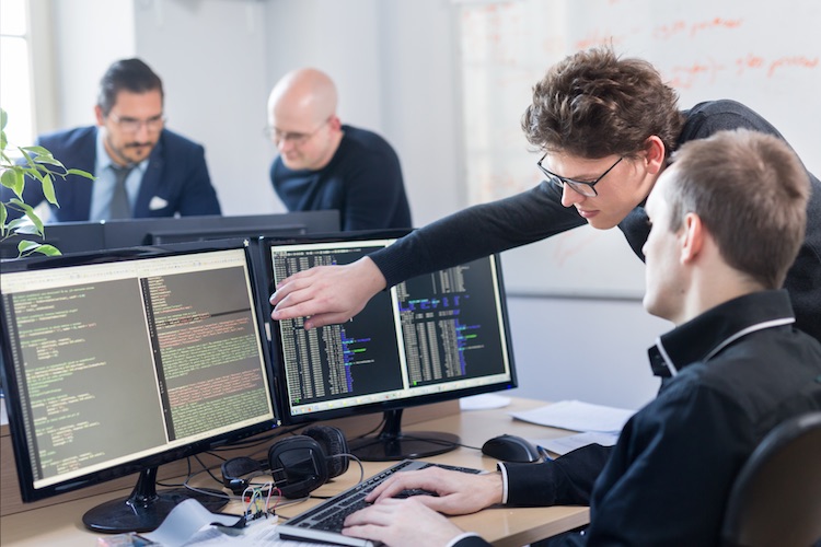 Two information assurance engineers review software code on a screen.