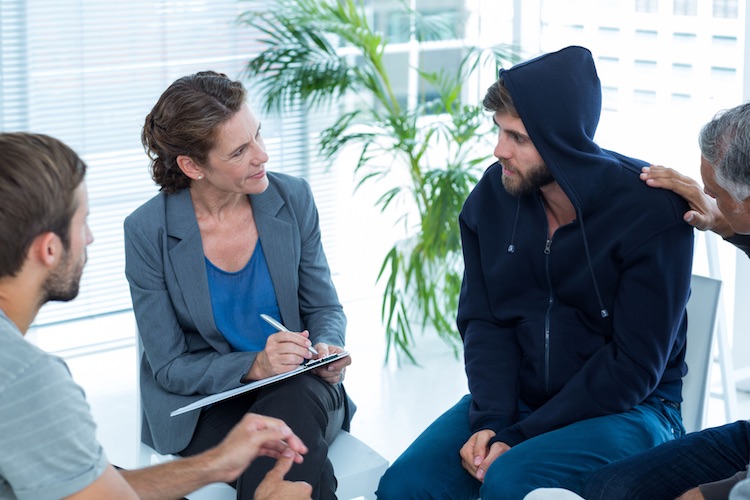 Female counselor in group setting evaluates patient while writing notes down on her clipboard