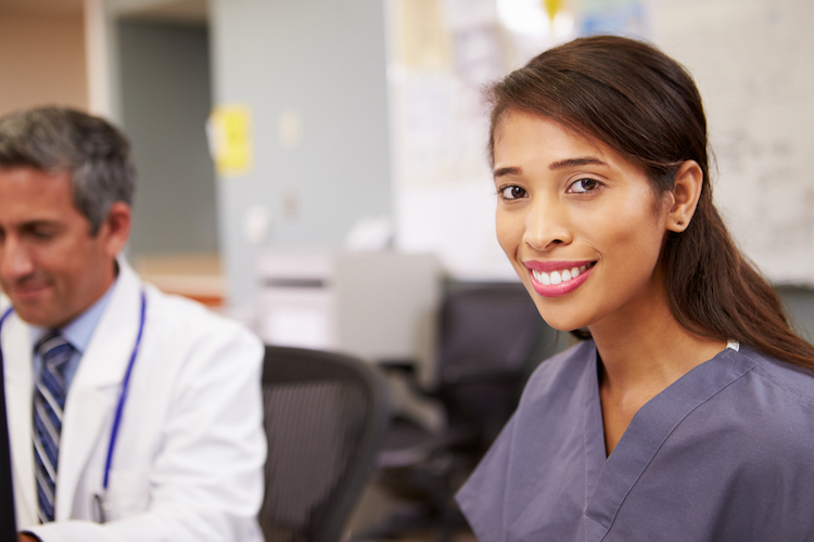 Portrait Of Female Nurse Smiling At Camera Whilst Working At Nurses Station