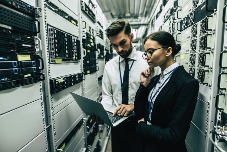a man and a women looking at a laptop in a server room