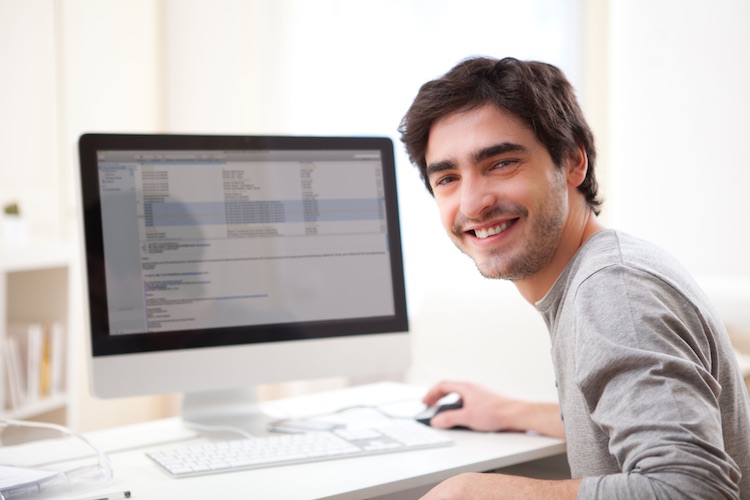 a smiling man sits at a desk with a computer in front of him