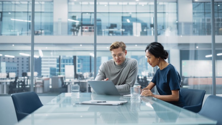 An IT manager working with an IT specialist at a table in an office.