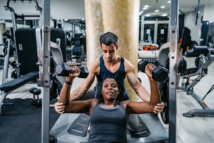 A personal trainer spots a client lifting weights.