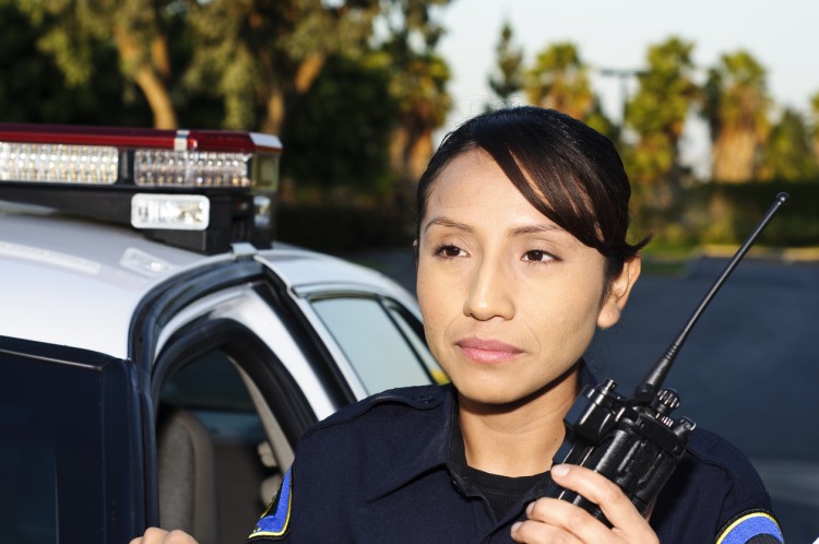 A police officer standing beside a patrol car and holding a hand-held radio.