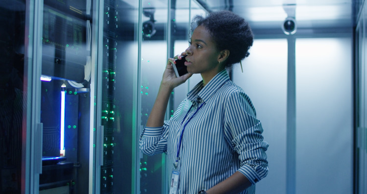 A networker administrator speaks on a cellphone in a server room.