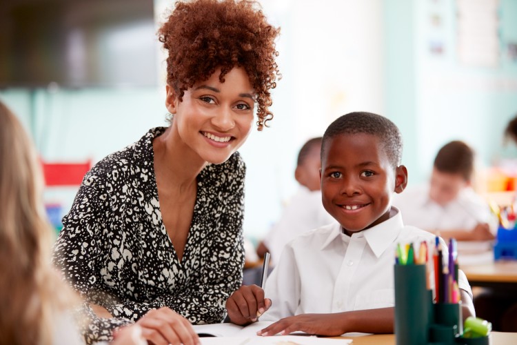 A smiling teacher works with an elementary student.