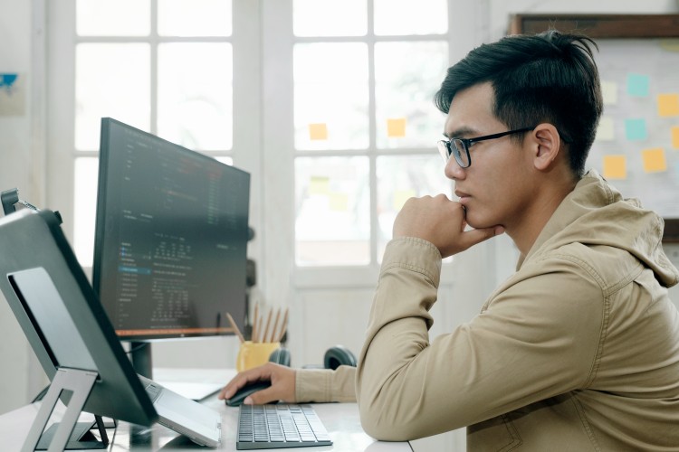 UX developer working on a dual-monitor computer system at a desk.