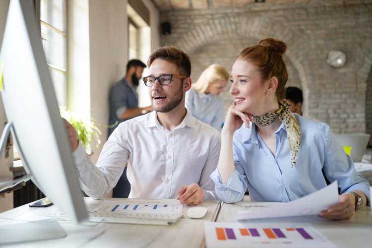 A VP of marketing sits at a desk and works on a project with a coworker.