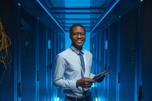 A smiling cybersecurity professional stands in a data center.