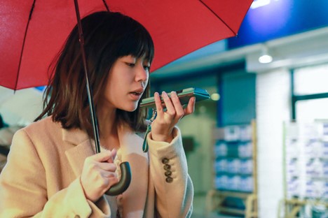 A woman holding an umbrella uses a smartphone’s voice recognition technology.