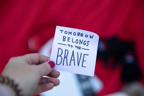 hand holding white sticky note tomorrow belongs to the brave