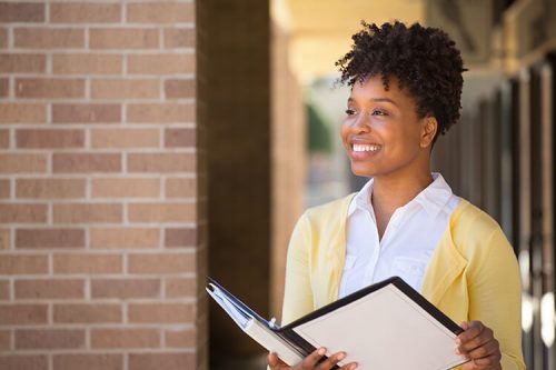 woman smiles outside building while holding binder
