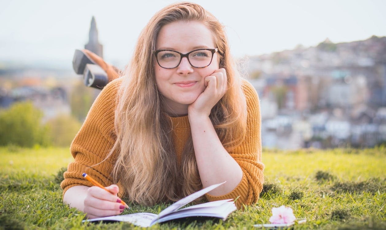 A female college student lying in a field doing homework