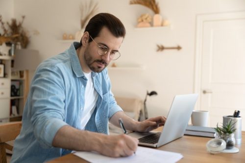 A graduate student takes notes while viewing an online lecture.