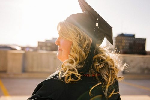 A woman with curly blonde hair wearing a graduation cap and gown