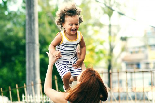 A redheaded woman playfully holds her smiling baby up in the air